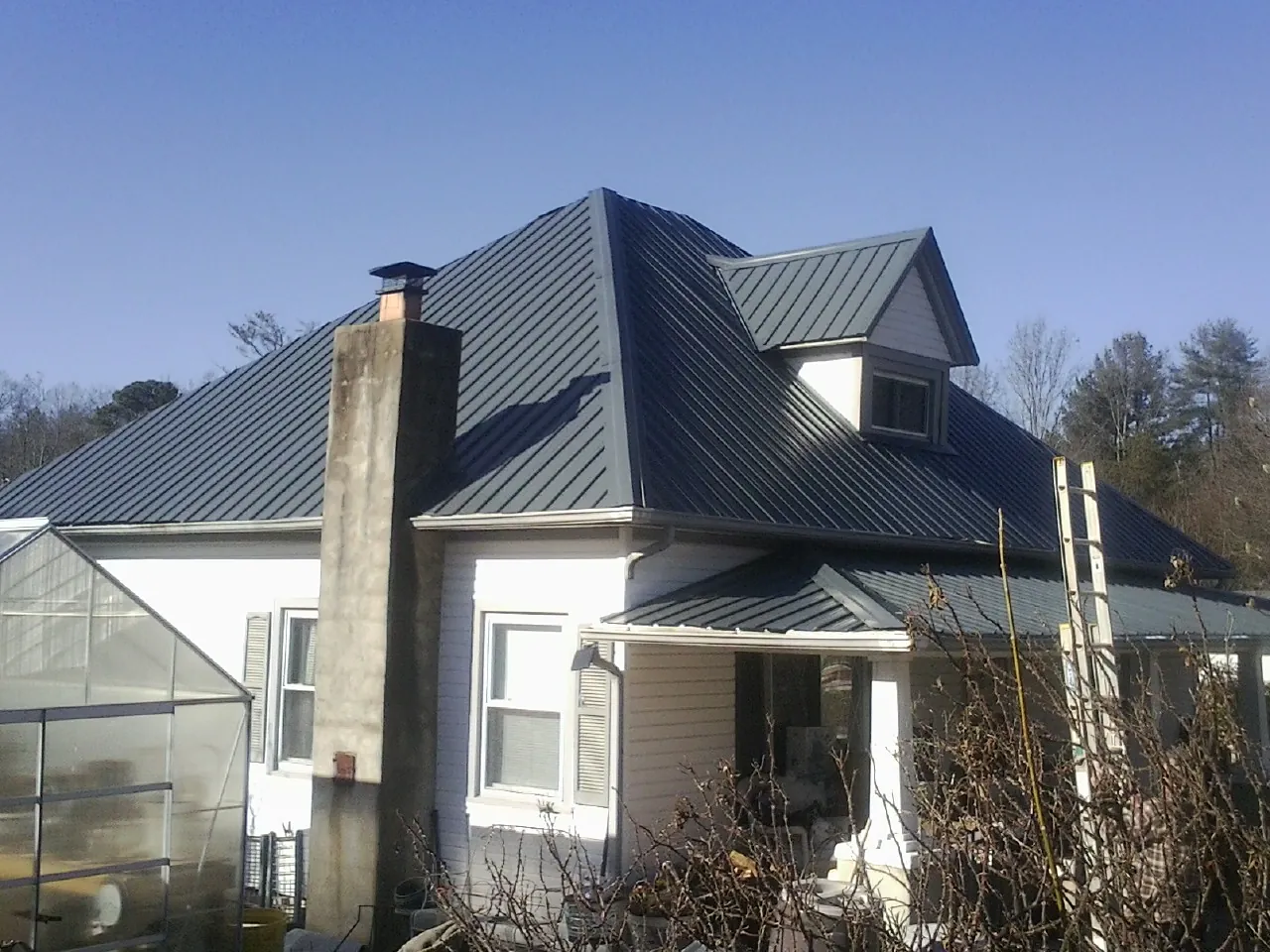 Dark blue standing seam metal roof on a white farmhouse with dormer in Pleasantville