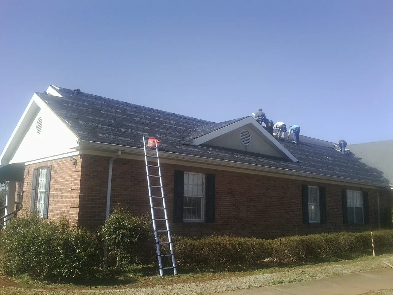 Crew tearing shingles off a brick ranch roof with a ladder set — Metal Roof Repair work by our crew in Pleasantville