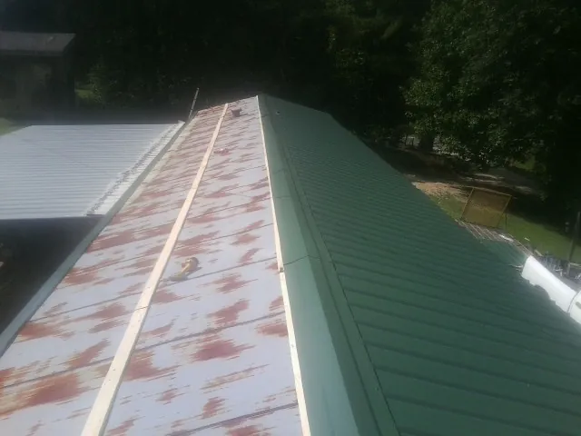 Old rusted panels beside newly installed green metal roofing — Wind Damage Roof Repair by Roofing Brothers in Pleasantville
