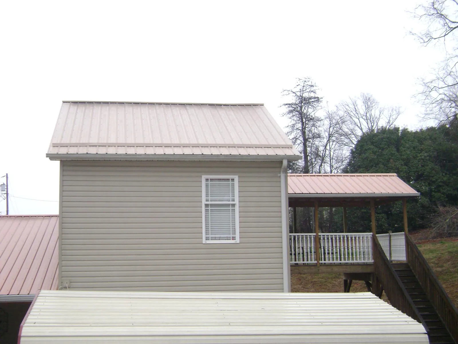 Tan metal roofs on a two story addition and attached porch, from a Roof Replacement job in Pleasantville